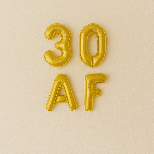 Gold inflatable balloons spelling '30 AF' on a beige background