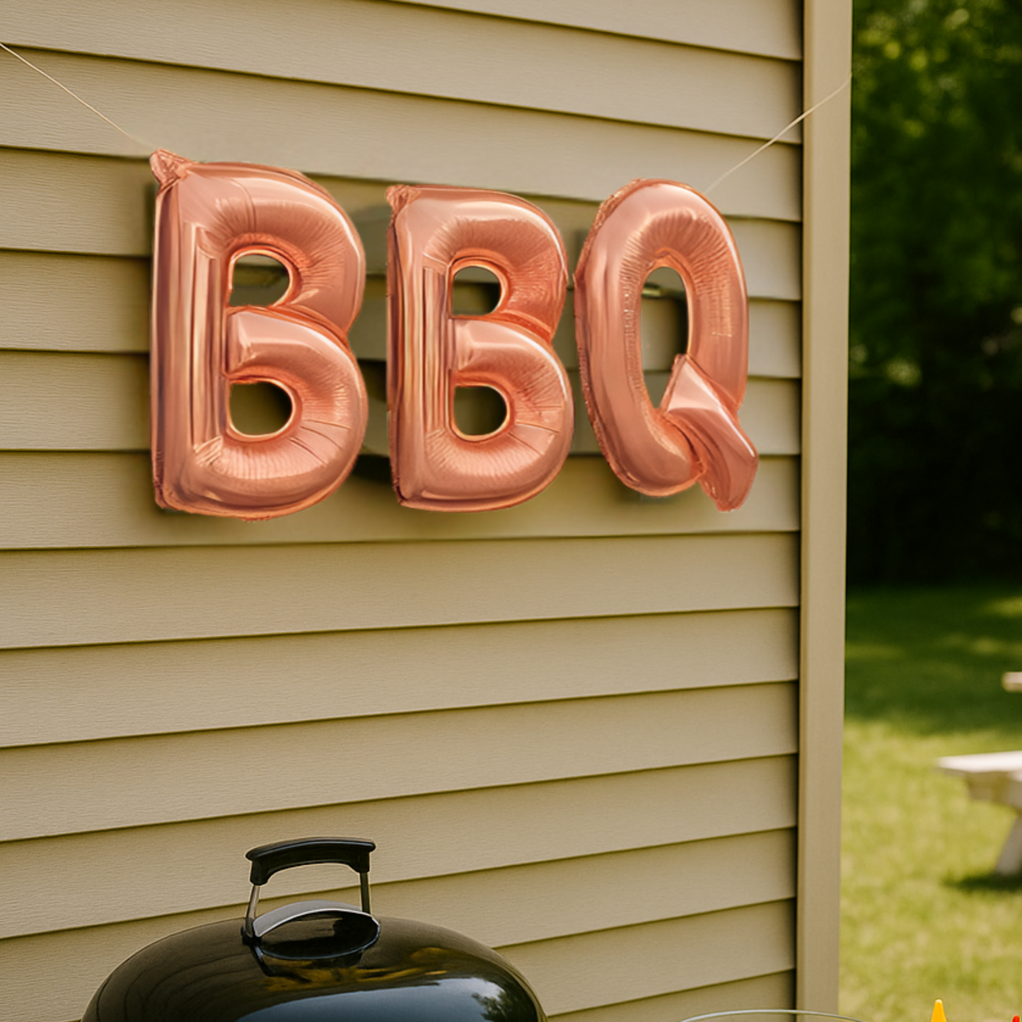 Rose gold 'BBQ' balloons attached to a house exterior with a barbecue grill in the foreground.