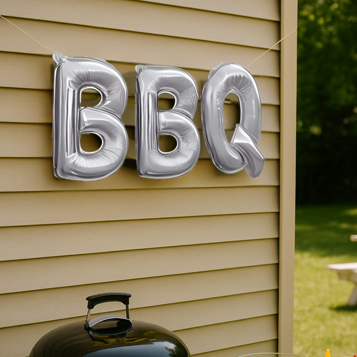 Silver 'BBQ' balloons attached to a wall with a barbecue grill in the foreground.