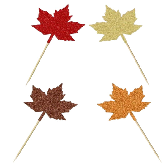Cupcakes topped with glitter maple leaf decorations in red, gold, orange, and brown, styled for Thanksgiving or Friendsgiving dessert tables.