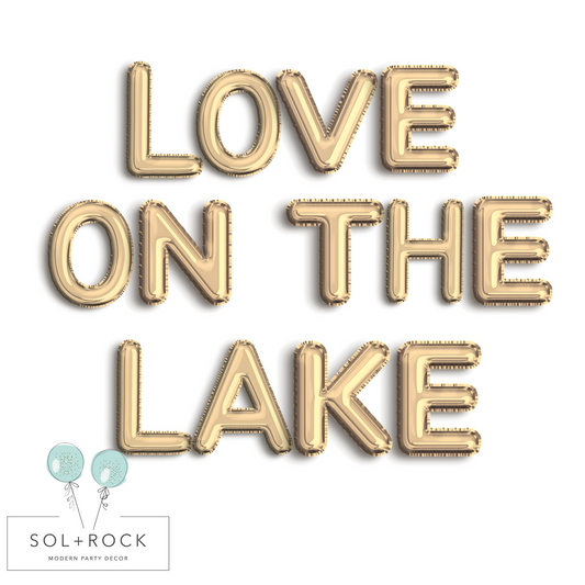 Gold balloon letters spelling 'LOVE ON THE LAKE' with Sol+Rock logo below on a white background