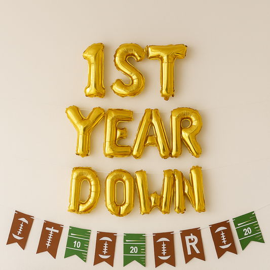 Gold foil balloons spelling '1st Year Down' on a beige background with football-themed bunting.