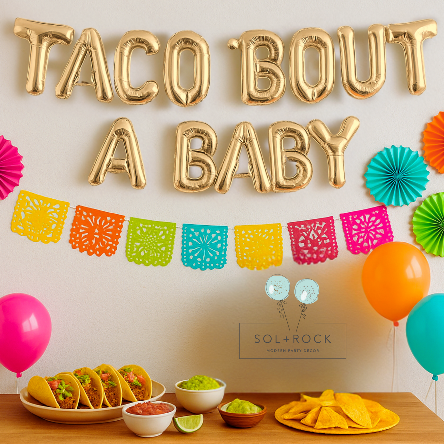 Decorative setup with 'Taco Bout A Baby' balloons, colorful balloons, and food items on a table.