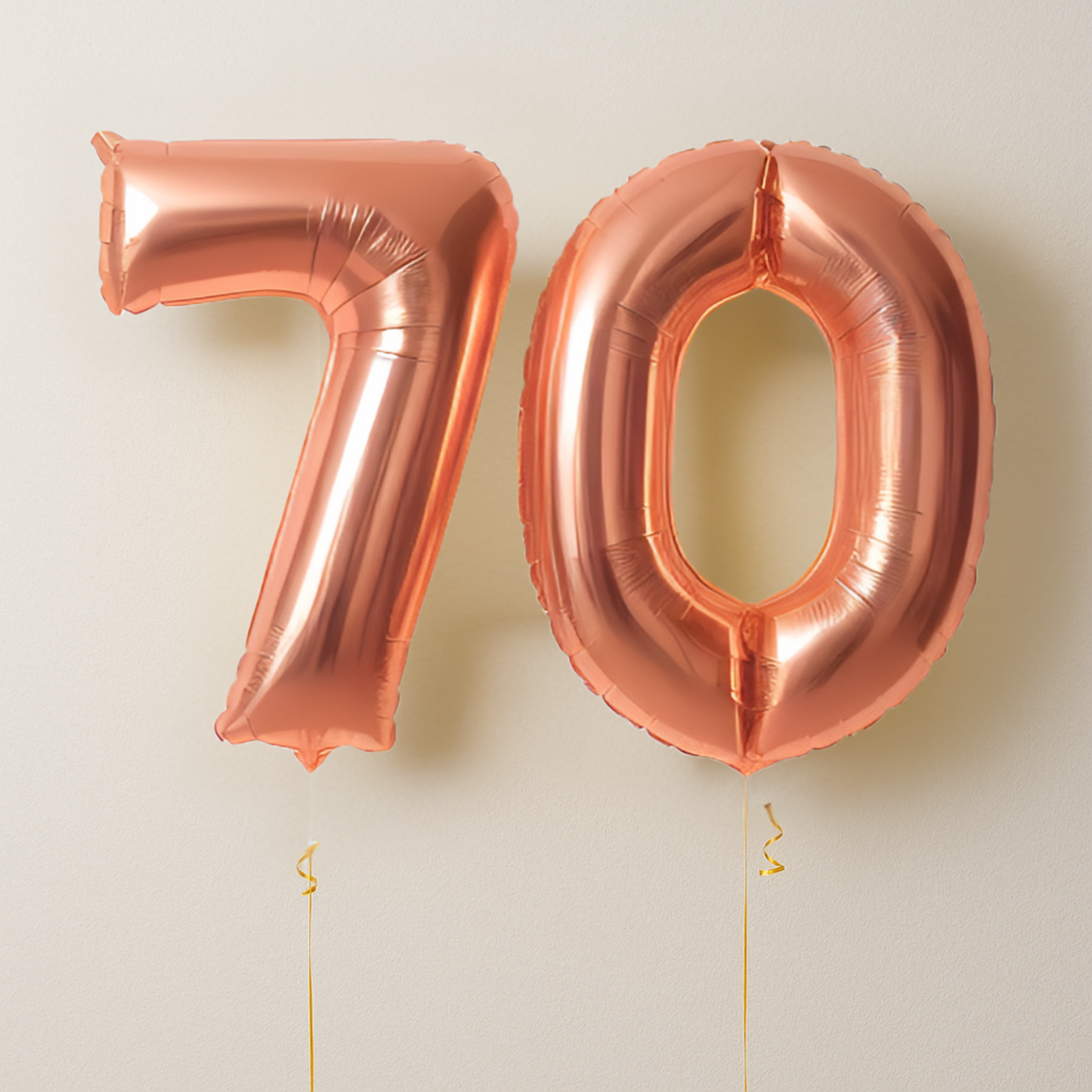 Rose gold number balloons spelling '70' on a light beige background