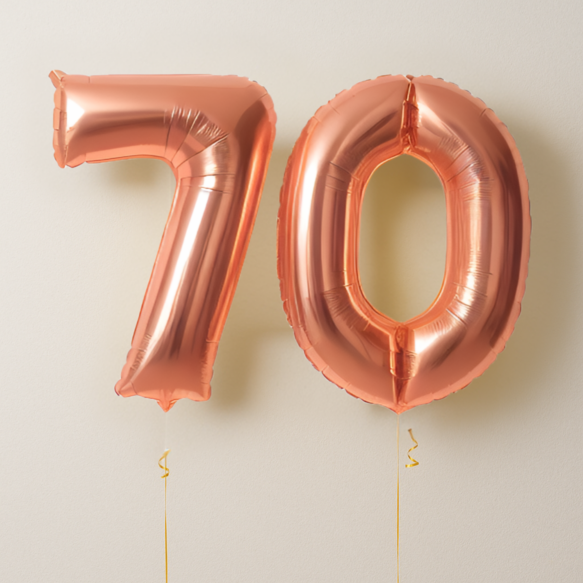 Rose gold number balloons spelling '70' on a light beige background