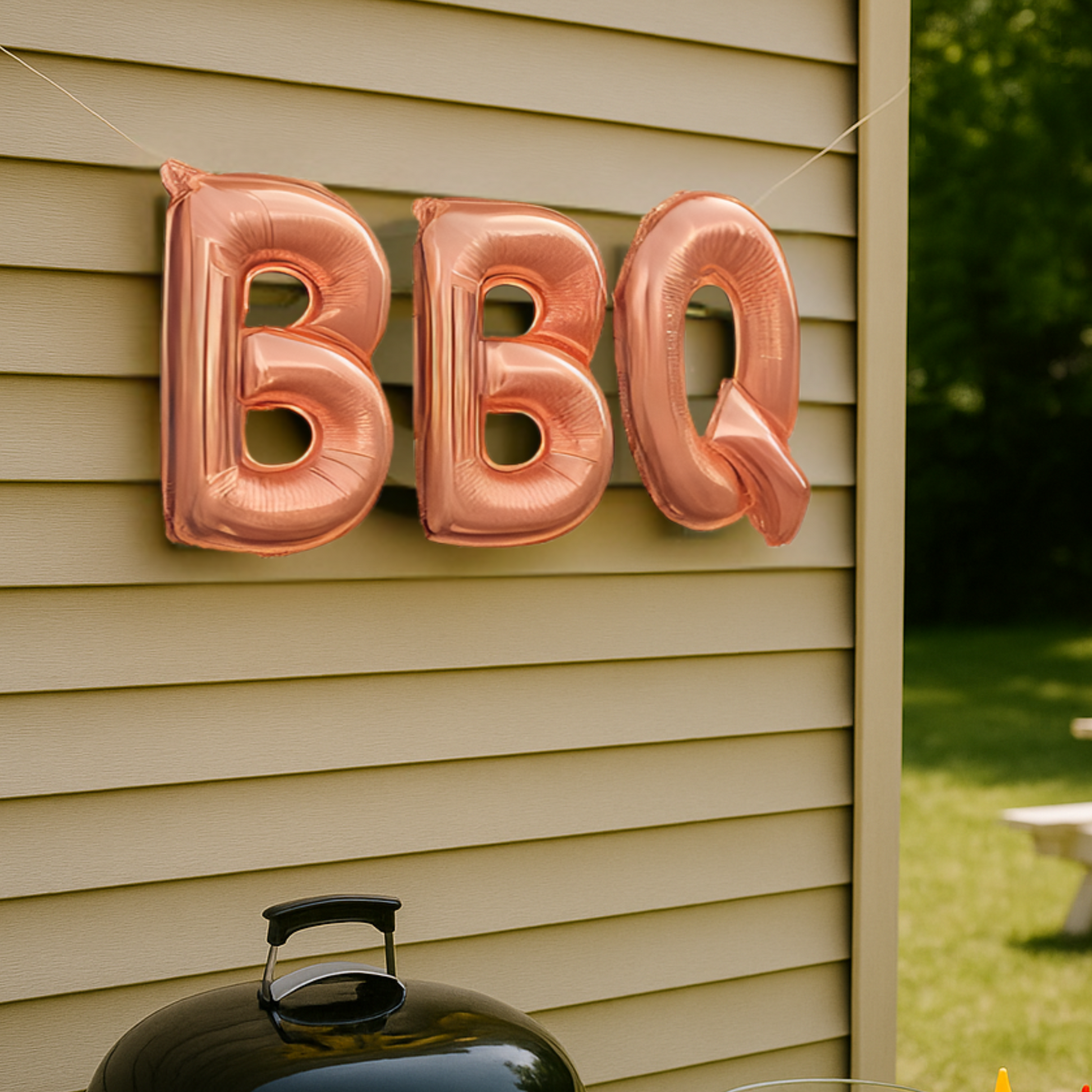 Rose gold 'BBQ' balloons attached to a house exterior with a barbecue grill in the foreground.
