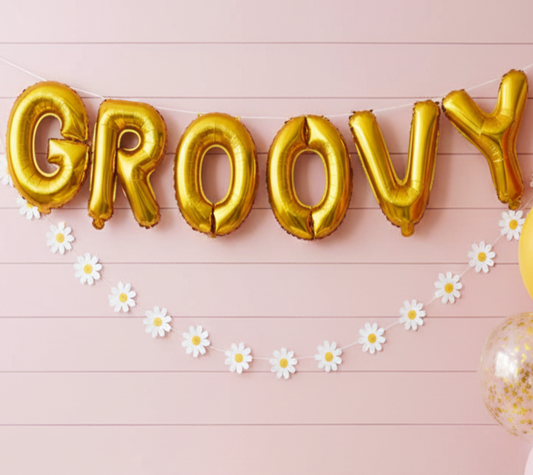 Decorated room with 'Groovy' balloons, balloons on a stand, and a cake on a table.