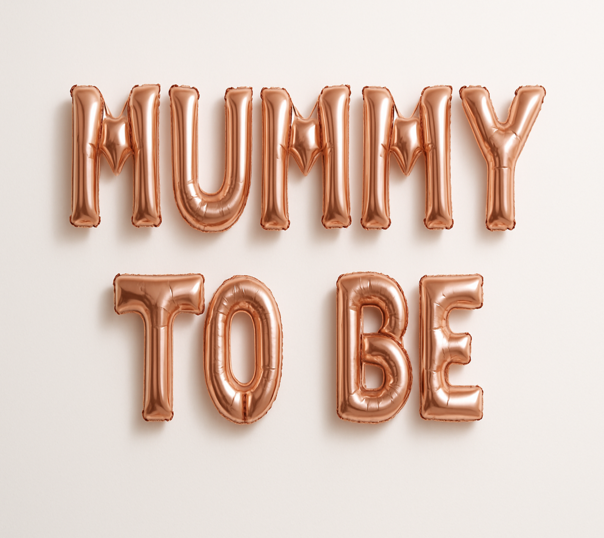 MUMMY TO BE in rose gold foil letter balloons on white background. 
