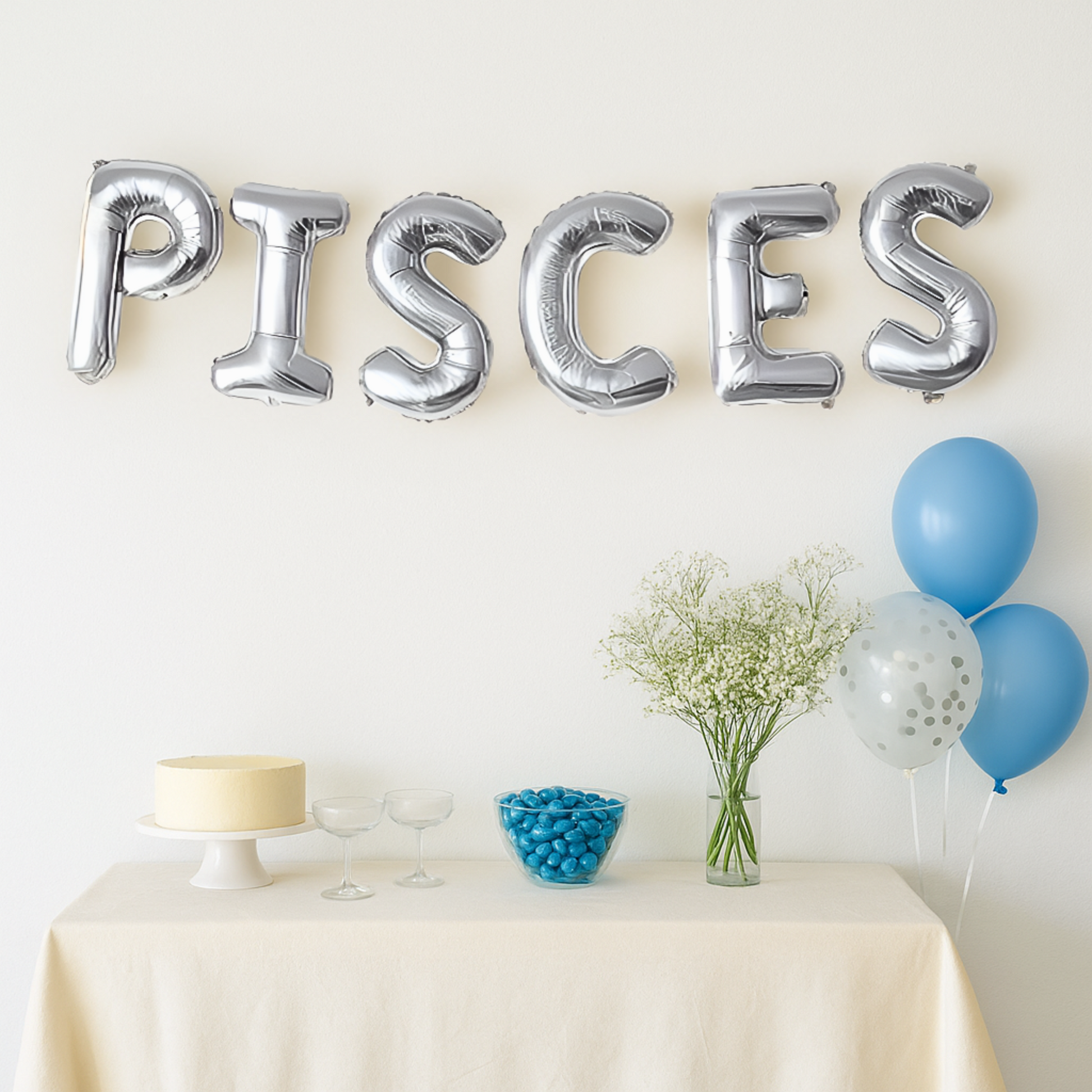 Silver 'PISCES' balloons above a table with decorative items on a light background