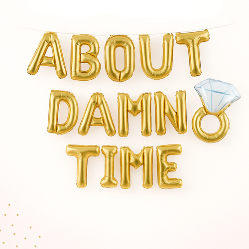 Gold foil balloons spelling 'ABOUT DAMN TIME' with a diamond ring balloon.