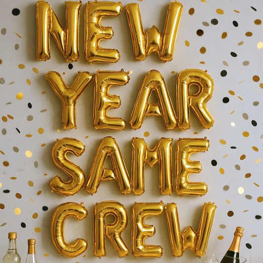 Gold foil balloon banner spelling New Year Same Crew on party wall